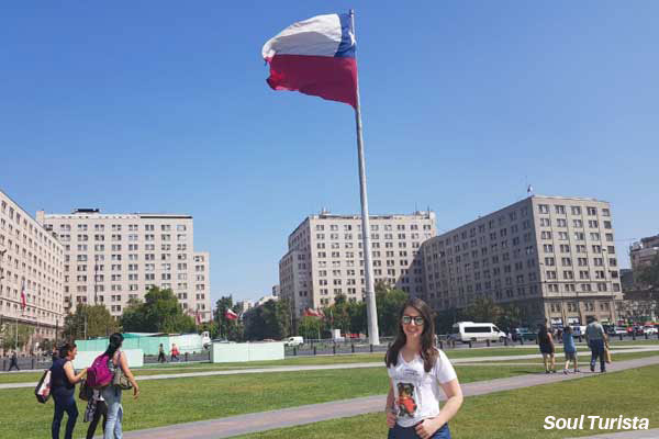 Minha foto na praça em frente ao Palácio com a enorme bandeira do Chile ao fundo