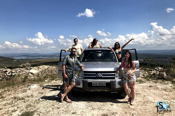 Cinco amigos em torno de um carro 4x4 com uma paisagem das montanhas de Minas Gerais ao fundo