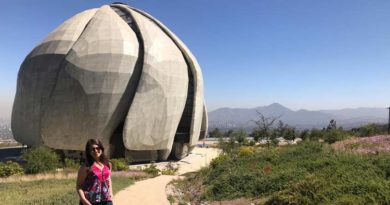 Minha foto em frente a construção do templo Bahai feita em mármore em dia ensolarado. Nos jardins, vegetações circulando o caminho e a Cordilheira dos Andes ao fundo