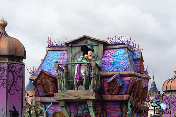 Carro roxo e temático de dia das bruxas com o Mickey vestido de bruxo acenando para os visitantes do parque