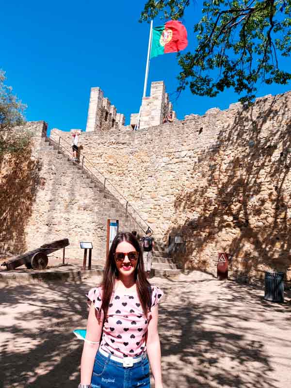 Eu nas muralhas do Castelo de São Jorge. Ao fundo, está a bandeira de Portugal