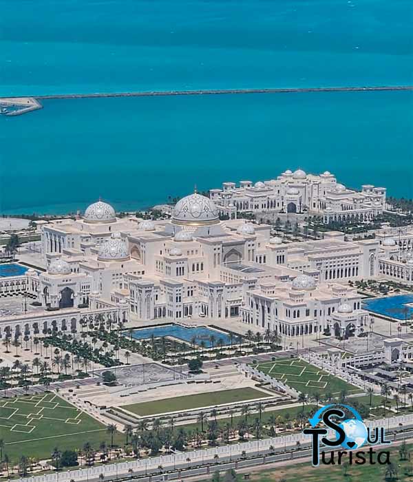 Vista de cima do enorme Palácio Presidencial Qsar Al Watan visto pela janela do mirante das Torres Etihad. Ao fundo, está um mar de azul muito brilhante