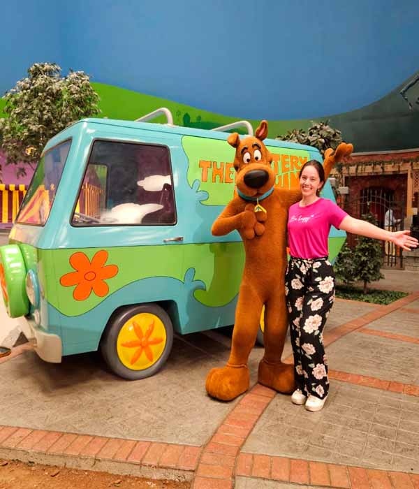 Visitar o Parque da Warner Bros é uma das coisas mais legais pra quem procura o que fazer em Abu Dhabi. Nessa foto, está eu e o Scooby Doo sorrindo para a câmera. Eu estou de braços abertos. Ao fundo, está o carro azul e verde que ele usa para caçar os inimigos junto com a Turma do Scooby Doo