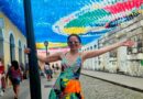 Eu me pendurando em um poste e abrindo os braços e um corredor de bandeirinhas juninas no céu de São Luís do Maranhão