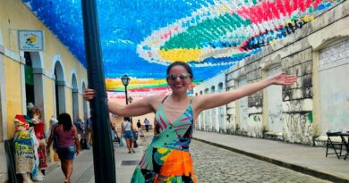 Eu me pendurando em um poste e abrindo os braços e um corredor de bandeirinhas juninas no céu de São Luís do Maranhão